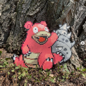 Pokémon Slowbro Perler bead artwork sitting on grass at the base of a large tree.
