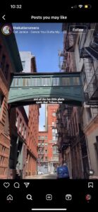 Screenshot from Instagram featuring a photo New York City. In the Image there is a green enclosed pathway that connects 2 buildings. Behind the pathway you can see blue skies and red brick buildings. There are subtitles written in white font in the middle of the screen that read: "and all the fun little photo spots Tribeca has."
